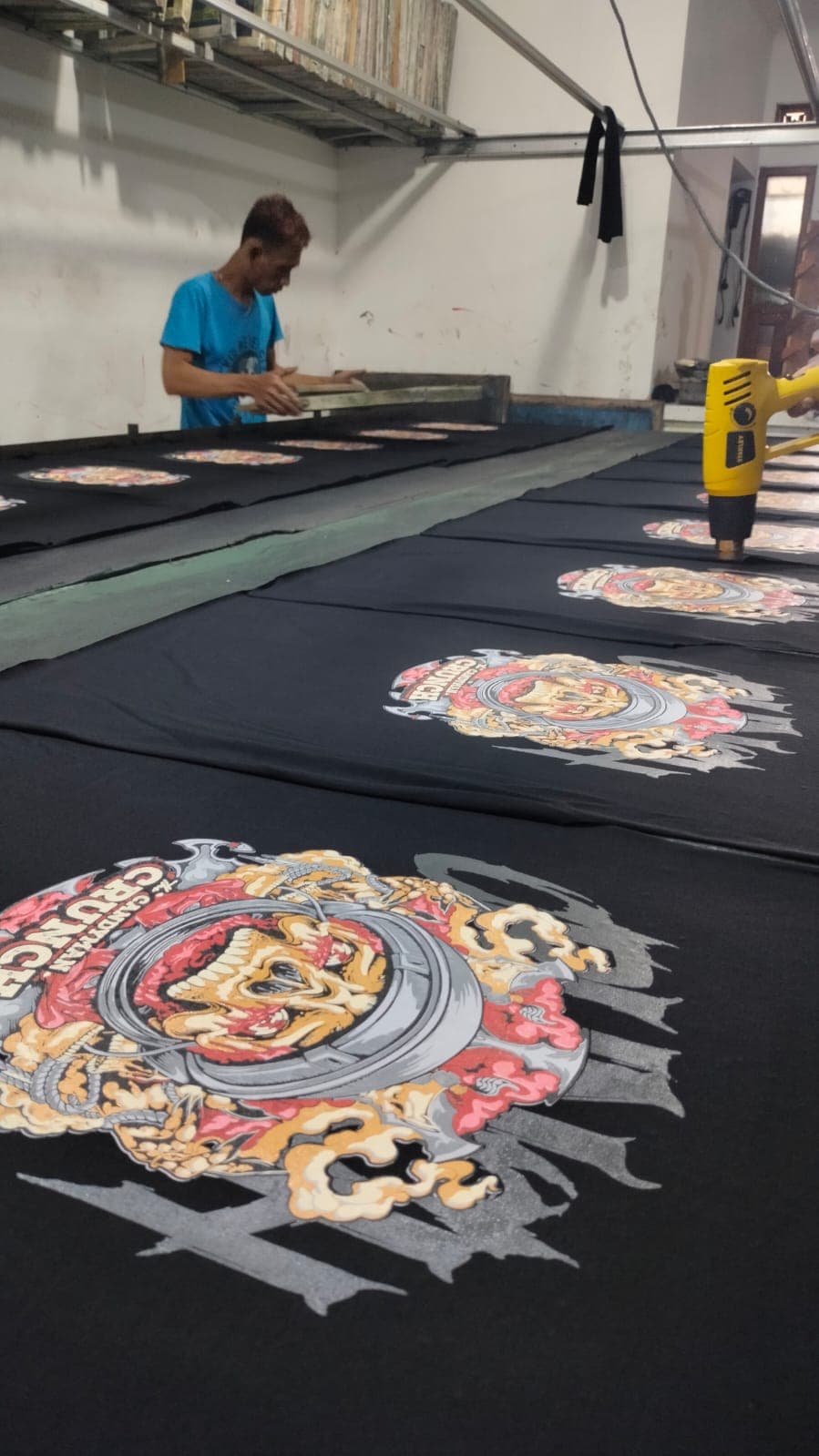 Proses sablon manual pada beberapa kaos hitam di meja produksi